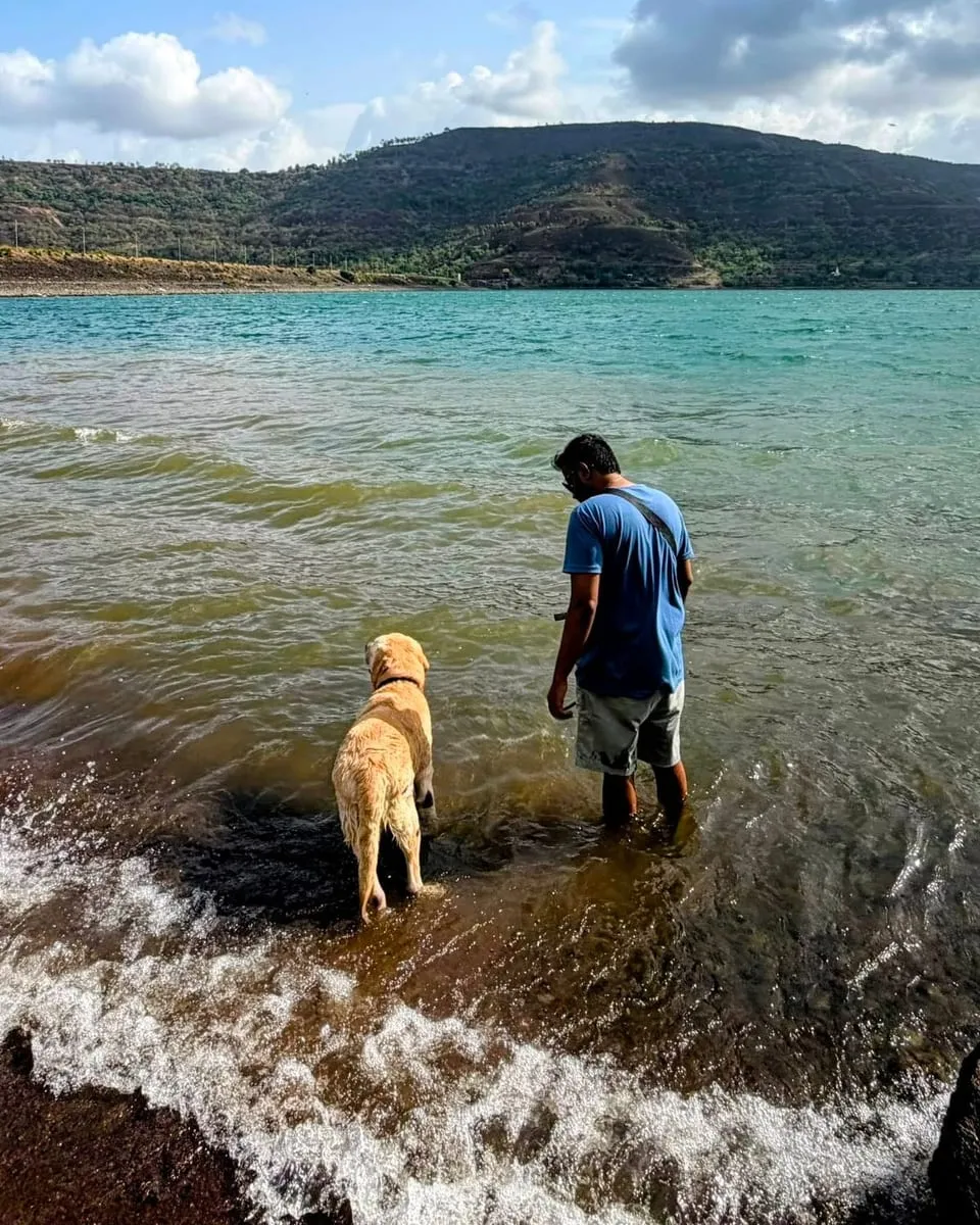 Akash and Aalloo standing in the shallows of a lake, with green hills behind