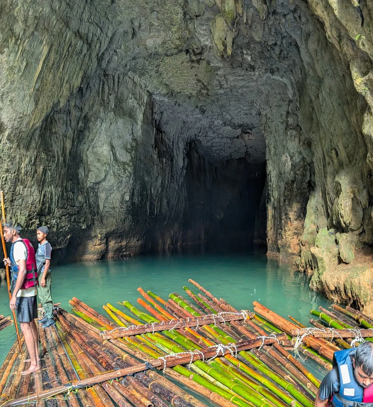 Bamboo rafts on turquoise water at the mouth of a cave