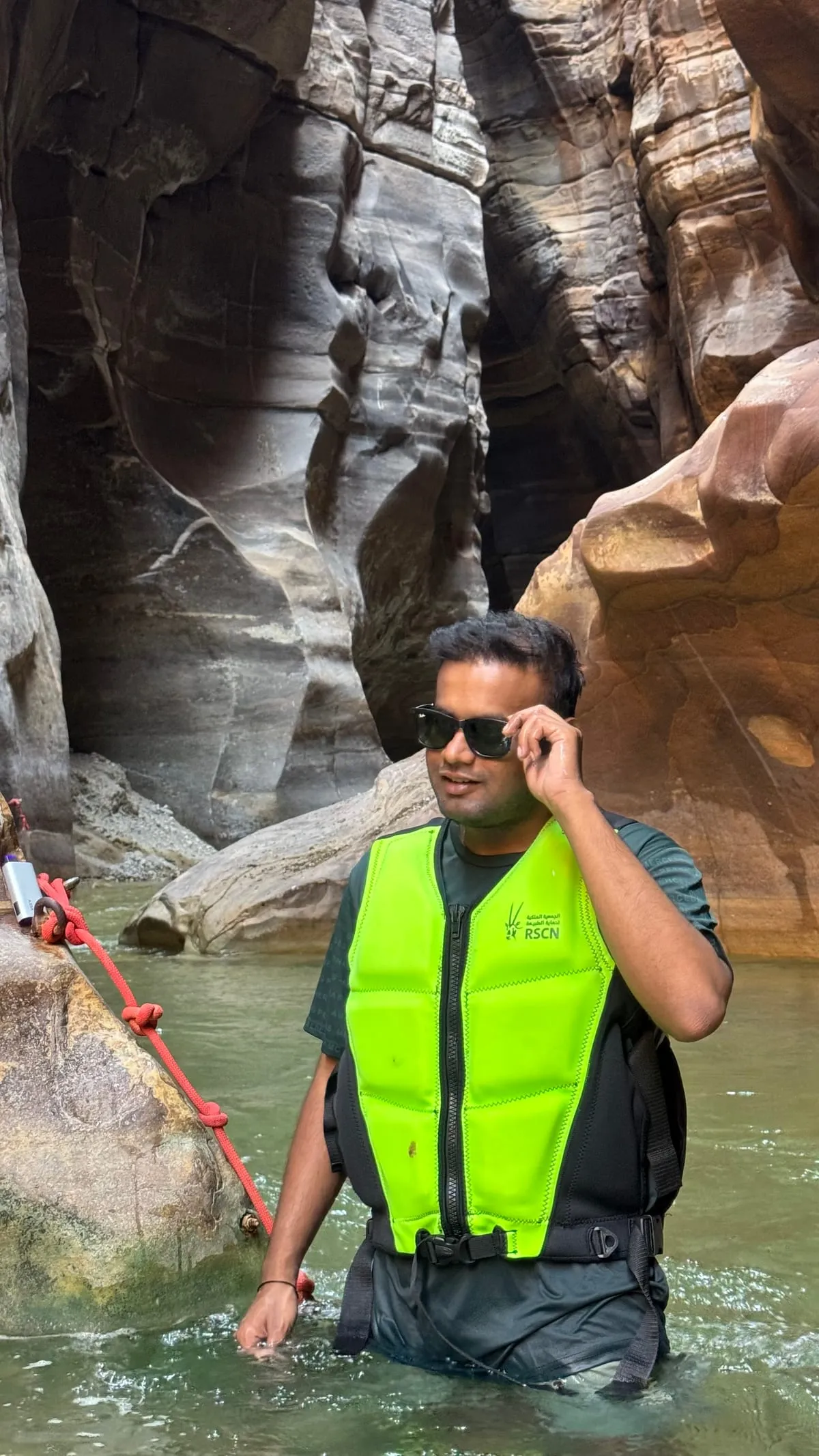 Akash in a life jacket, waist-deep in the river between the canyon walls of Wadi Mujib