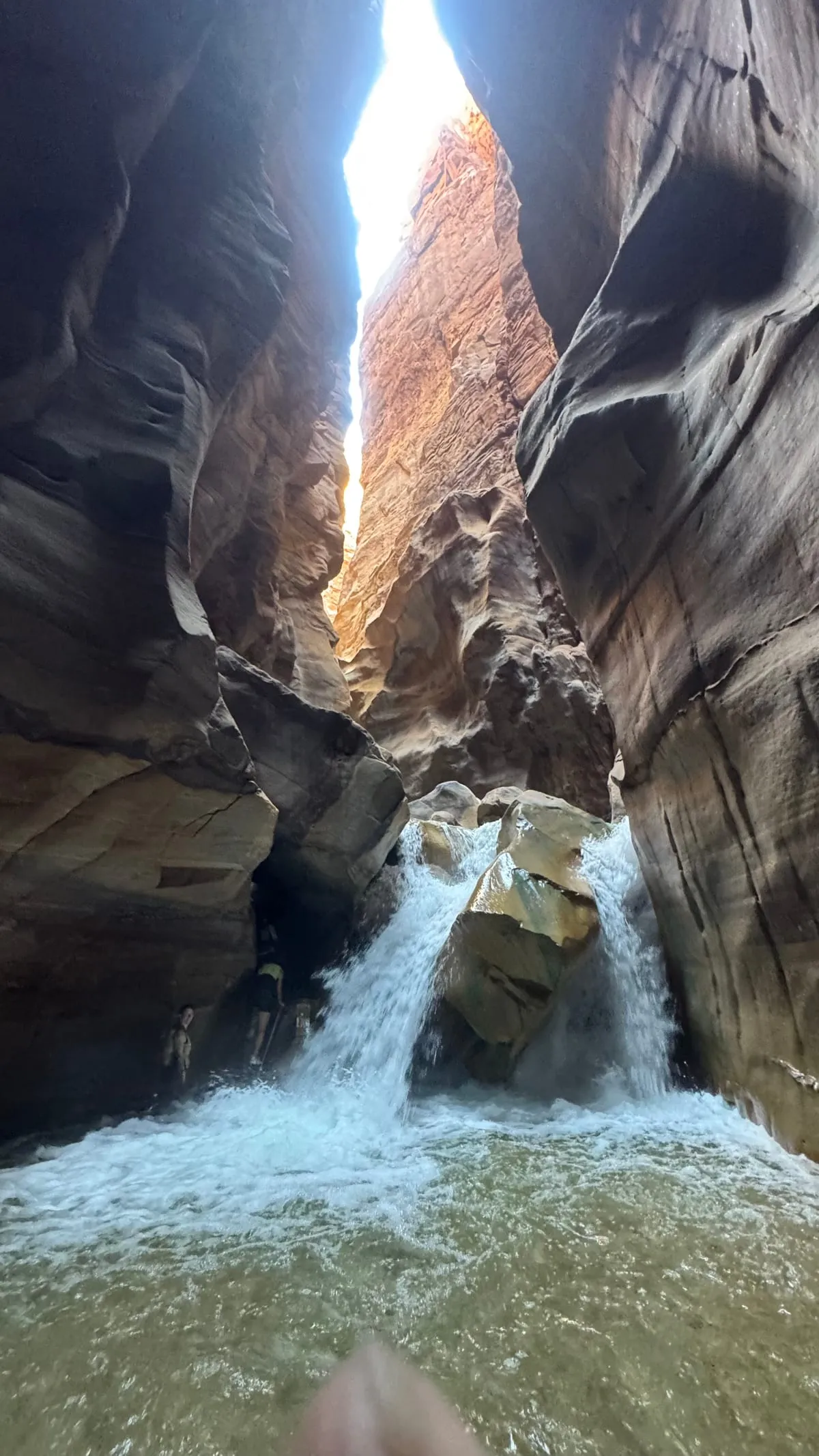 A waterfall pouring through a narrow gap in the sandstone at Wadi Mujib